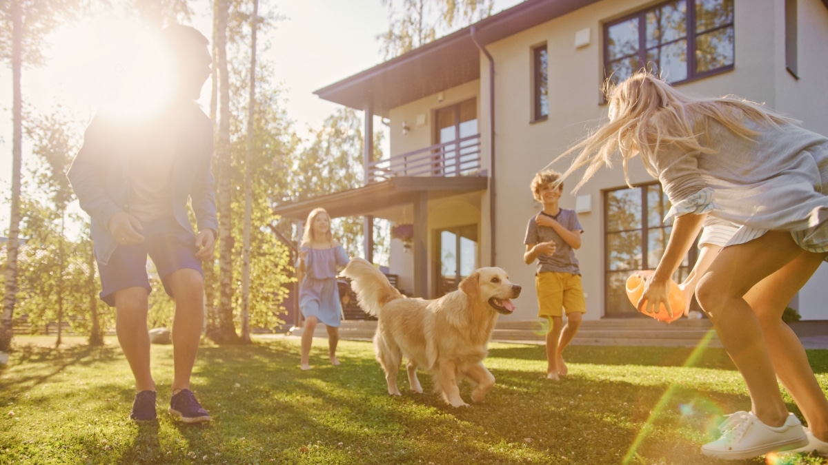 Children and parents playing with their dog outside a well-kept home with maid service.